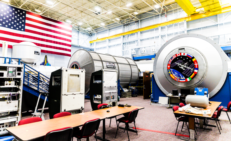 ISS mockup with example racks that fit into the curves of each module sitting behind the chairs.